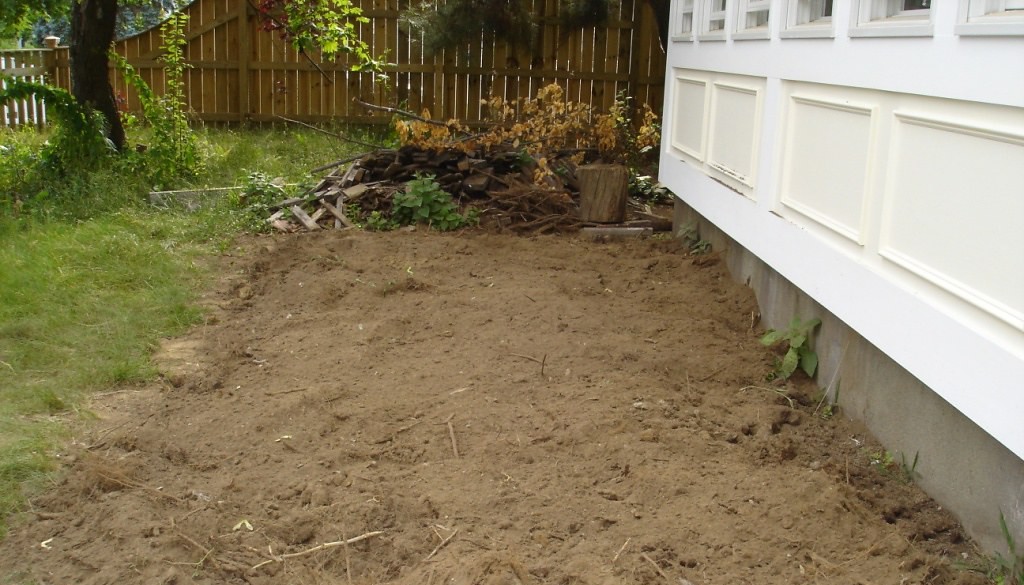 Area beside a house cleared of vegetation down to bare, loose brown soil