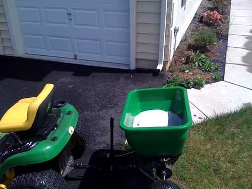 Tow-behind broadcast spreader loaded with granular lawn product next to a lawn