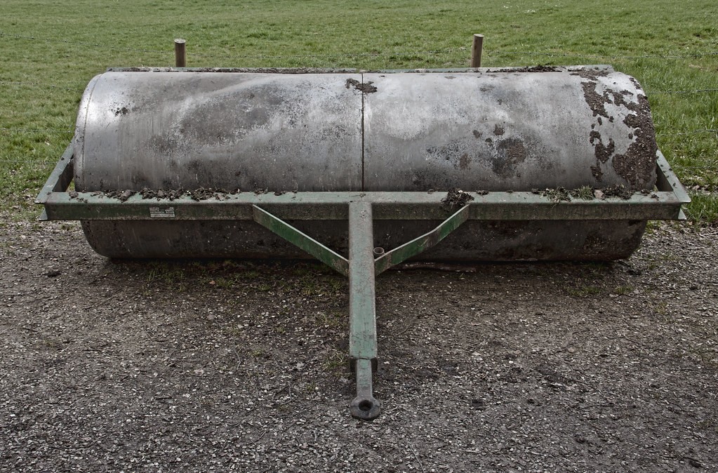 Heavy metal drum roller with a tow frame parked on gravel beside a grass field
