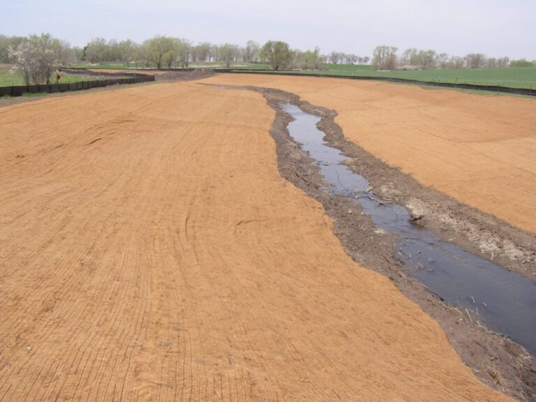 Long bare banks either side of a small creek completely covered with tan erosion-control blankets laid in overlapping strips