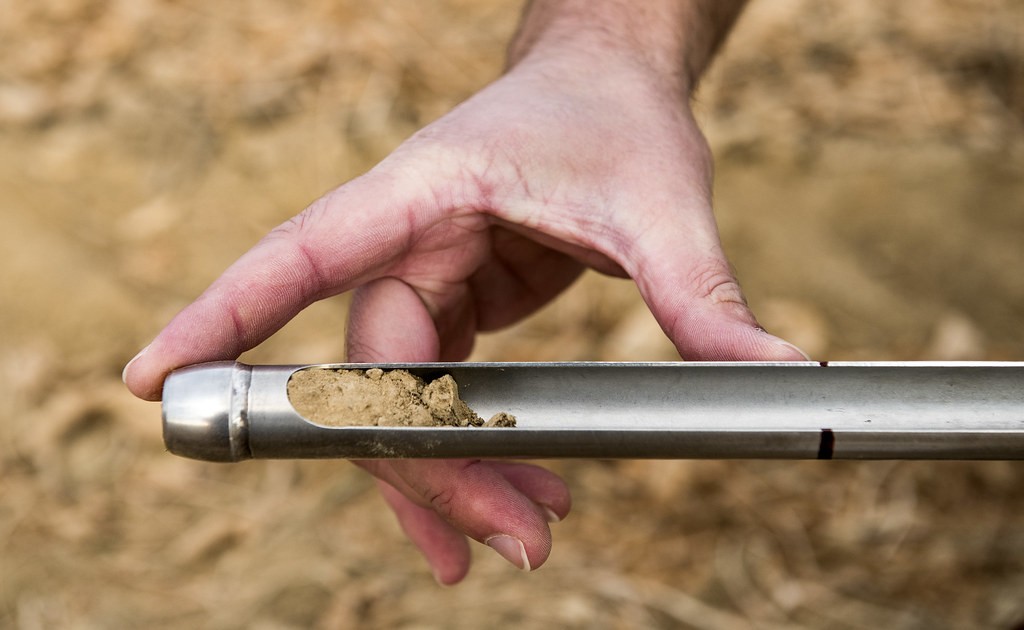 Hand holding a stainless steel soil probe with a core of soil in its slot